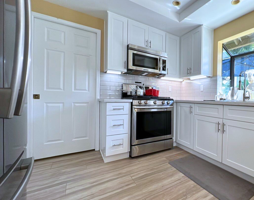 A modern kitchen with white cabinets, stainless steel appliances, subway tile backsplash, and wood-look flooring.
