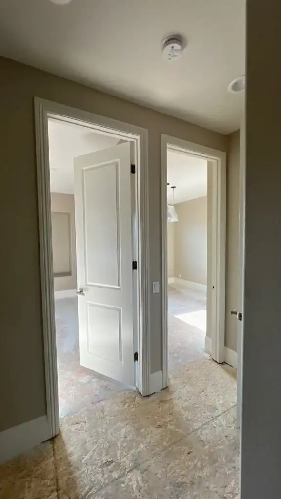 Interior view of a hallway with open doors leading to unfinished rooms, showcasing flooring installation progress for residential spaces.