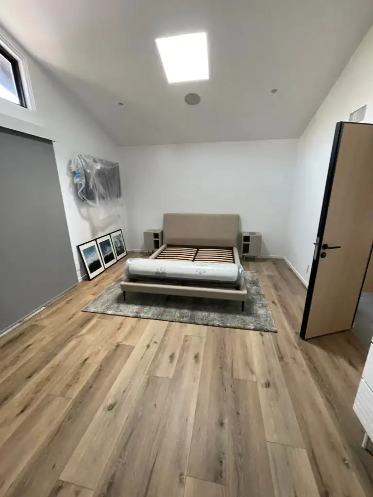 Modern bedroom with hardwood flooring, unmade bed on a rug, framed artwork on the wall, and natural light from a skylight, showcasing Sparkle Restoration's flooring installation services.