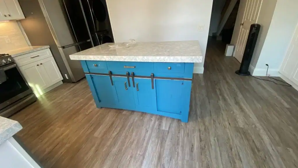 Kitchen island with blue cabinetry and granite countertop, surrounded by light wood flooring, showcasing a modern kitchen environment.