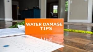 Water damage tips sign on a wooden floor with measuring tape and documents, relevant to expert advice for handling water damage insurance claims for Orange County homes.